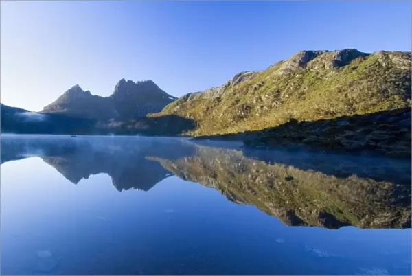 Mountain scenery - stunning Dove Lake in front of massive Cradle Mountain is one of Tasmania's most beautiful and famous natural features. In early morning there is still mist on the calm waters of Lake Dove