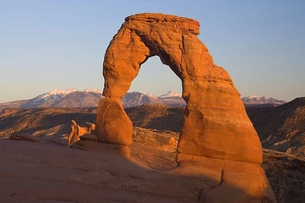 Delicate Arch - delicately sculptured sandstone arch standing in front of snow-covered Manti-La Sal Mountains on a slickrock slope. In late evening - Arches National Park, Utah, USA