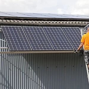 Two engineers installing photovoltaic solar PV panels on roof of steel barn Cotswolds UK