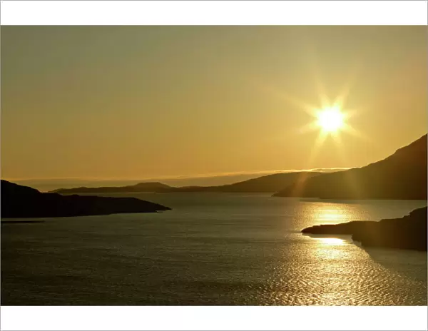 Sunset over Loch Broom with sun still up casting red light over water and mountain ridges around the Loch Loch Broom near Ardmair, Wester Ross, Highlands, Scotland, UK