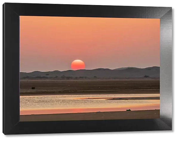 Middle East, Arabian Peninsula, Ash Sharqiyah South, Jalan Bani Buali. Sun setting over hills and coastal marsh in Oman. Date: 27-10-2019
