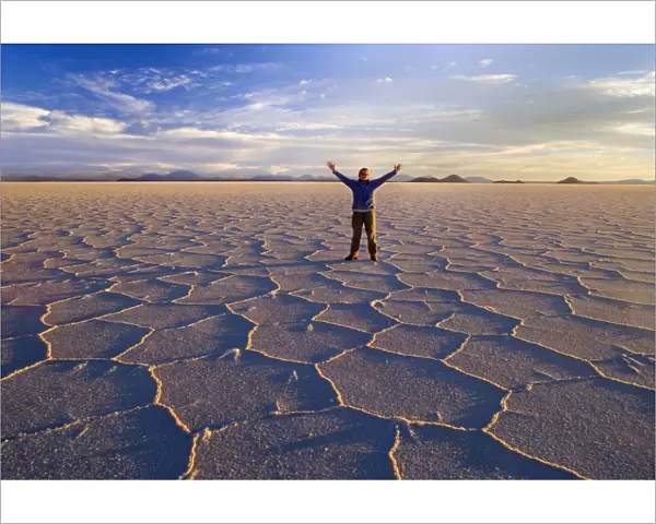Traveller on Salar de Uyuni - a happy woman with raised hands stands amidst polygonal salt pattern on dried up salt lake at sunset - Salar de Uyuni - Altiplano - Bolivia - South America