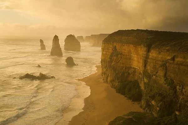 Twelve Apostles - a storm is brewing over the coastline and fragile sandstone stacks of the Twelve Apostles. The low sun is able to cut through a hole in the thick clouds and casts an eerie yellow light onto the cliffs, the ocean and the sky