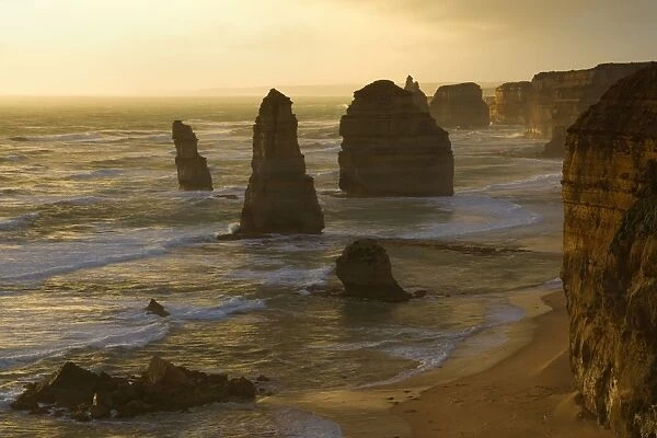 Twelve Apostles - a storm is brewing over the coastline and fragile sandstone stacks of the Twelve Apostles. The low sun is able to cut through a hole in the thick clouds and casts an eerie yellow light onto the cliffs