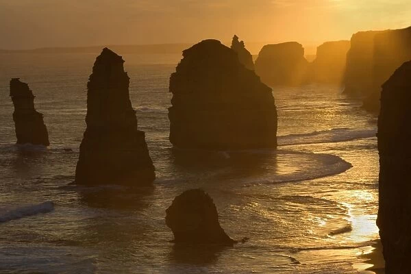 Twelve Apostles sunset - setting sun over the sandstone rock formations of famous Twelve Apostels, which are sculpted by the relentless sea. The force of the sea eats more and more of the rocks away and finally forces them to collapse