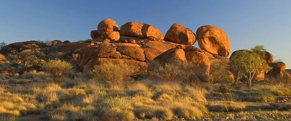 Devils Marbles - several circular shaped marbles of red granite are balanced on top of a hugh rock in last evening light. The whole rock formation is situated amidst grassy bushland - Devils Marbles Conservation Area, Northern Territory, Australia