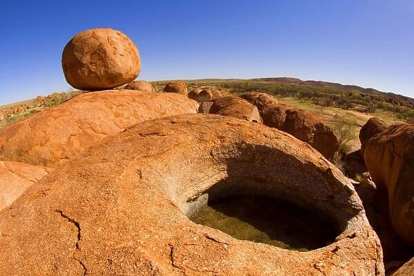 Devils Marbles - a nearly perfectly circular shaped boulder of red granite is balanced on a hugh rock with a small crevice filled with water - Devils Marbles Conservation Area, Northern Territory, Australia