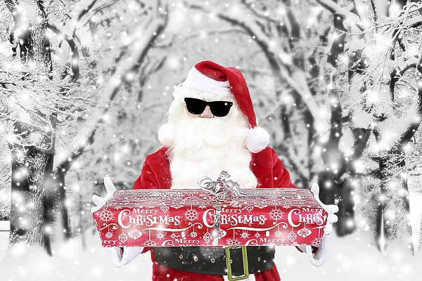 Father Christmas  /  Santa Claus wearing sunglasses holding Christmas present in winter snow