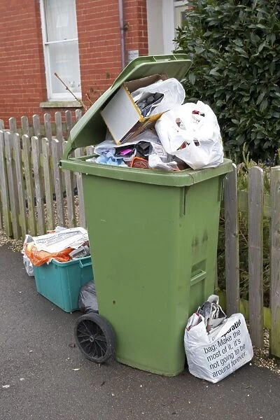 Green wheelie bin overflowing with domestic rubbish awaiting collection Cheltenham UK