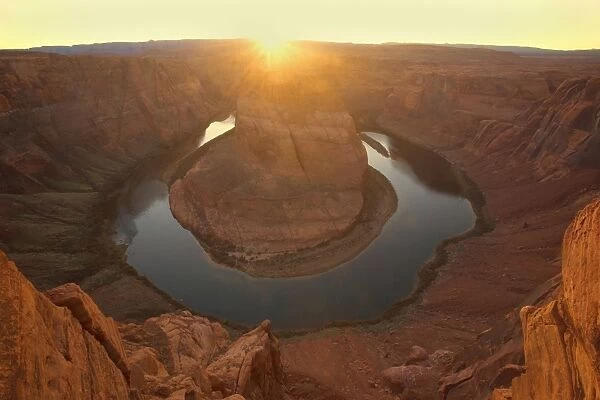 Horseshoe Bend - dramatic view of a nearly 360 degree bend of the Colorado river cut into the colorado plateau. At sunset, with the setting sun about to vanish behind the horizon - Horseshoe Bend, Arizona, USA