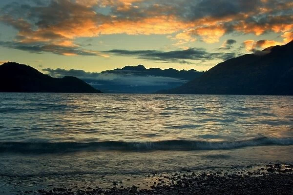 Lake Wakatipu - view towards the ragged mountain range of The Remarkables just before sunrise when the clouds are highlighted by the rising sun Queenstown, Otago, South Island, New Zealand