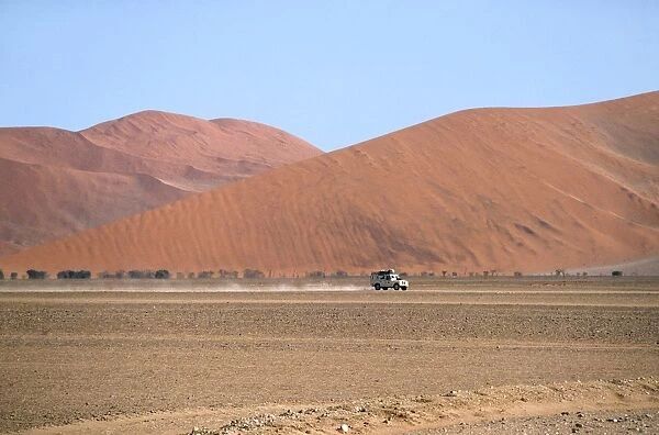 Namibia - a landrover drives through the valley at Sossusvlei flanked by mountainous dunes
