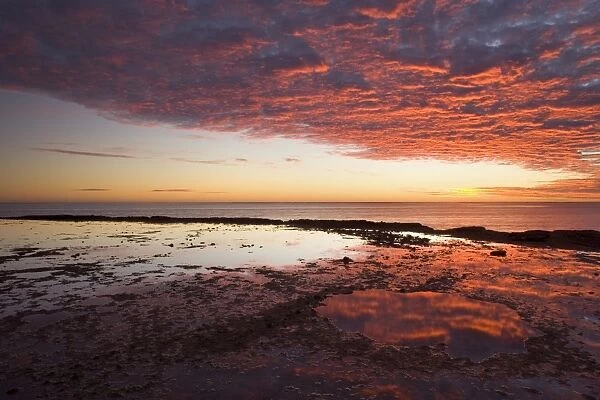 Ningaloo sunset - gorgous sunset over Ningaloo Reef and ocean. Brilliantly red ablaze clouds reflect in the calm surface of remaining water in rock pools - Ningaloo Reef Marine Park, Western Australia, Australia