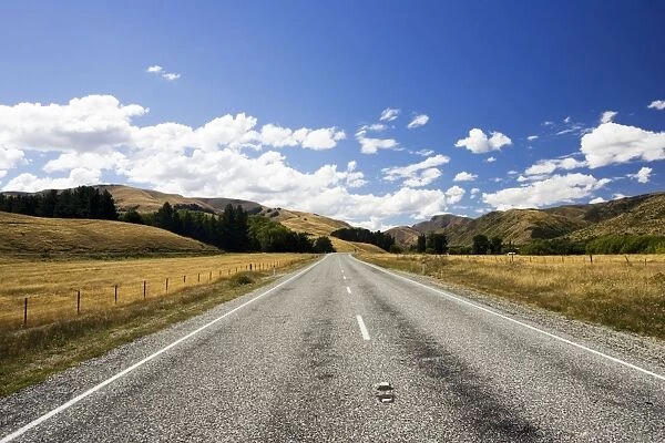 Road - long straight deserted tarmac paved road, rolling hills, white clouds, blue sky. Mackenzie country - New Zealand