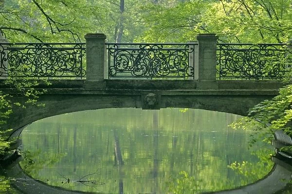 Romantic bridge in baroque style reflecting in brook in spring forest Park of Nymphenburg castle, Bavaria, Germany
