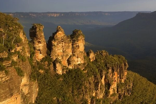 The Three Sisters - famous sandstone formations Three Sisters, seen from Echo Lookout, at sunset. The low sun finds a hole in the heavily clouded sky and plunges exactly the Three Sisters in exquisite red light - Blue Mountains National Park