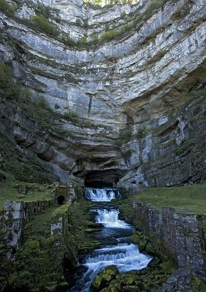 The source of the River Loue, where it emerges from a huge cave at the base of a jurassic limestone cliff. Jura, East France
