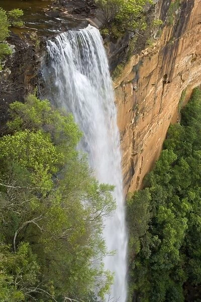 Tianjara Falls - view of stunning waterfall rushing over a red cliff from above. It plunges into a deep gorge, surrounded by lush forest - Moreton National Park, New South Wales, Australia