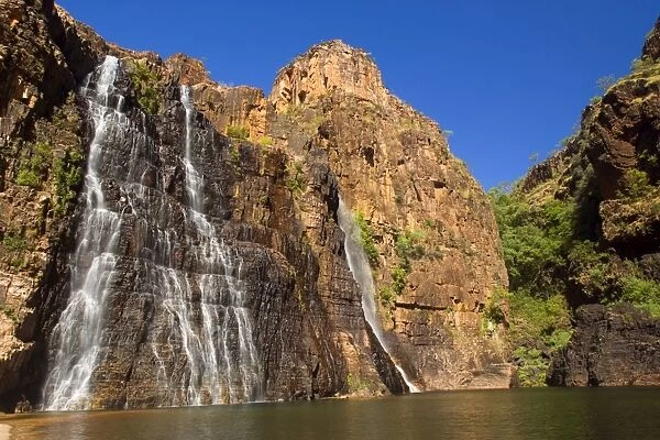 Twin Falls - water cascades down a steep cliff into a turquoise cloured pool which is surrounded by high, red cliffs - Kakadu National Park, Northern Territory, Australia