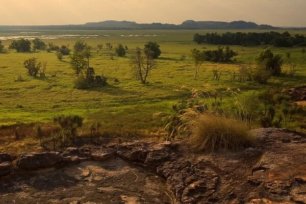 Ubirr view - breathtaking view from Ubirr rock towards the Nardab floodplain. The evening sun is partly hidden behind beautiful clouds and sends sunrays through the open gaps between the clouds