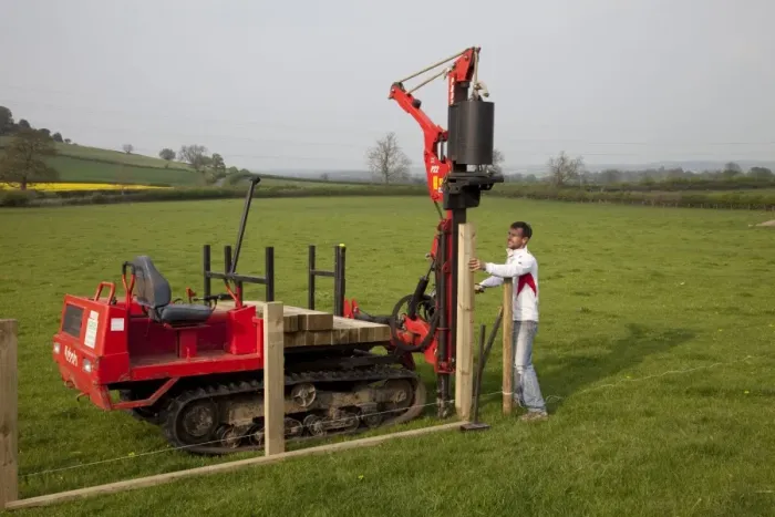 Framed Print : Workman driving timber posts into ground for new post and rail field fence with dedicated Kubota Protech tracked Post Rammer - Cotswolds - UK