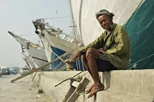 Behind Gallery: Boatman - sitting on wall - with Phinisi boats behind him