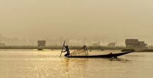 Burmese Fisherman fishing at dawn with village in