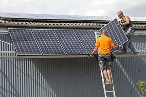 Alternative Energy Prints: Two engineers installing photovoltaic solar PV panels on roof of steel barn Cotswolds UK