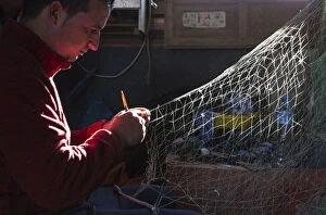 Fisherman repairs a net in his fishermans cottage