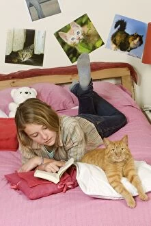 Girl lying on bed reading - with ginger cat lying