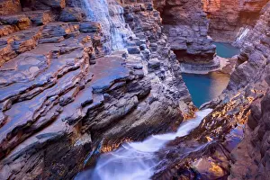 Hancock Gorge - water is flowing down a waterfall in Hancock Gorge into Raglan Pool and some further unaccessible pools beyond. They are surrounded by steep, red and very terraced cliffs