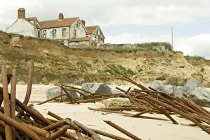 Defence Prints: Houses on cliff edge and remains old sea defences after severe coastal erosion Happisburgh North Norfolk Coast UK