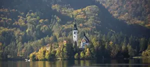Lake Bled. 14th - 17th century church on island in the lake, with autumn woodland colours on the mountainside beyond. Slovenia