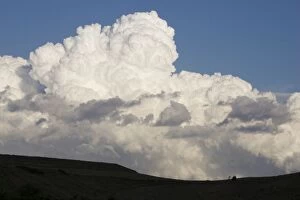 Low altitude billowing cumulus clouds on horizon looming above dark foreground