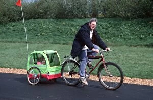 Man riding bicycle towing trailer with child