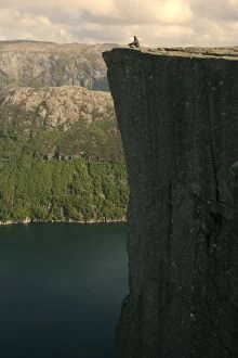 Preikestolen - person meditating near the edge of rock pulpit Preikestolen with vertical drop of nearly 600 m clearly