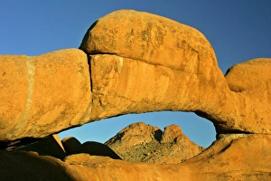 Rock arch - ablaze in late evening light framing Spitzkoppe mountain in background Rock arch - ablaze in late evening light framing Spitzkoppe mountain in background