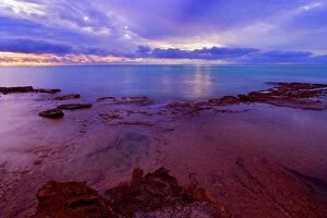 Sunset over the Reef - colourful sunset over Ningaloo Reef and the ocean. Heavy clouds darken the sky and give the picture a mystic touch. In the foreground there are ledges of the ragged exposed reef visible