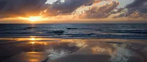 Tropical sunrise - the sun rises above the ocean at a tropical beach in North Queensland. The sun is partly hidden behind clouds and paints beautiful pastel colours, ranging from yellow to pink, in the sky